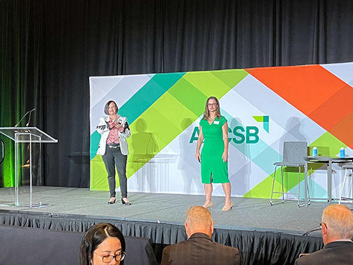 Two women stand on stage at AACSB conference giving presentation