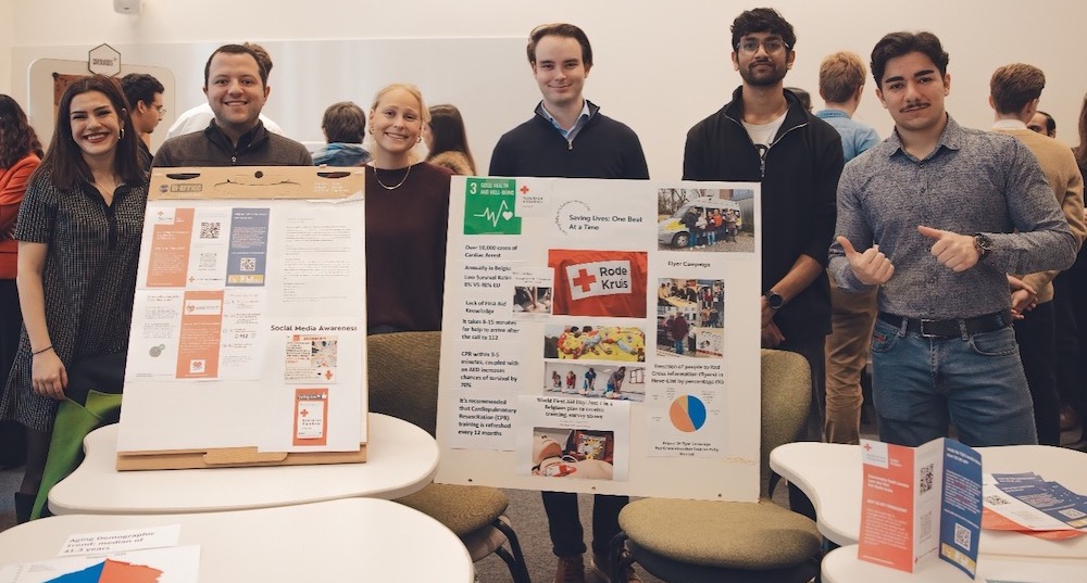 A group of students stand behind poster boards and brochures explaining the projects they have been working on.